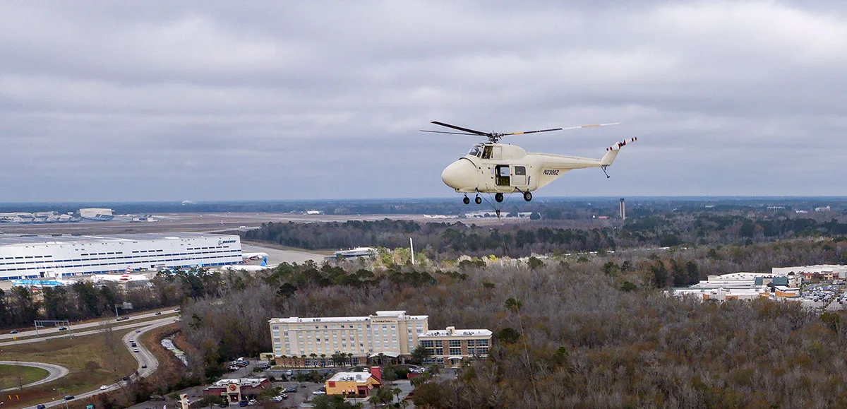Sikorsky S-55t helicopter skillfully hovering over North Charleston Coliseum during the precision exhaust fan replacement operation.