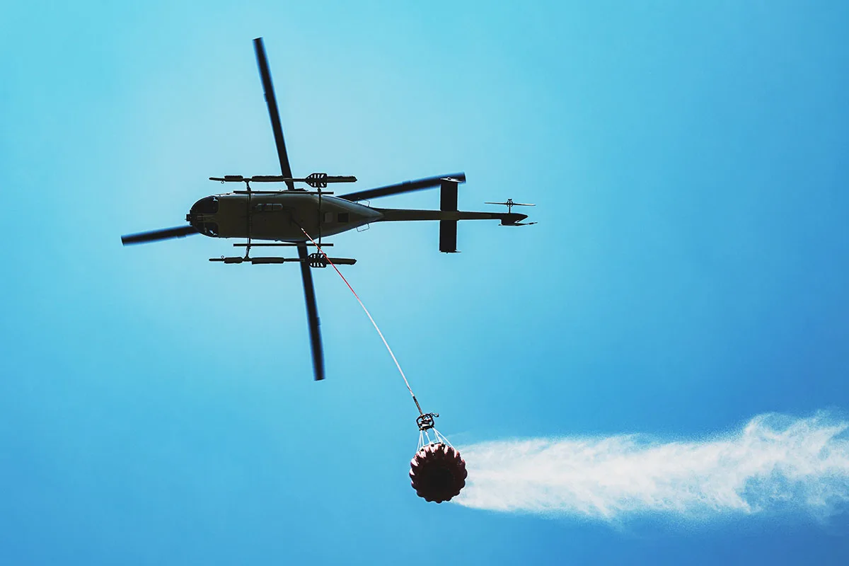 Helicopter performing slingload operation with a Bambi Bucket for aerial firefighting, demonstrating precision and skill in heavy lifting tasks