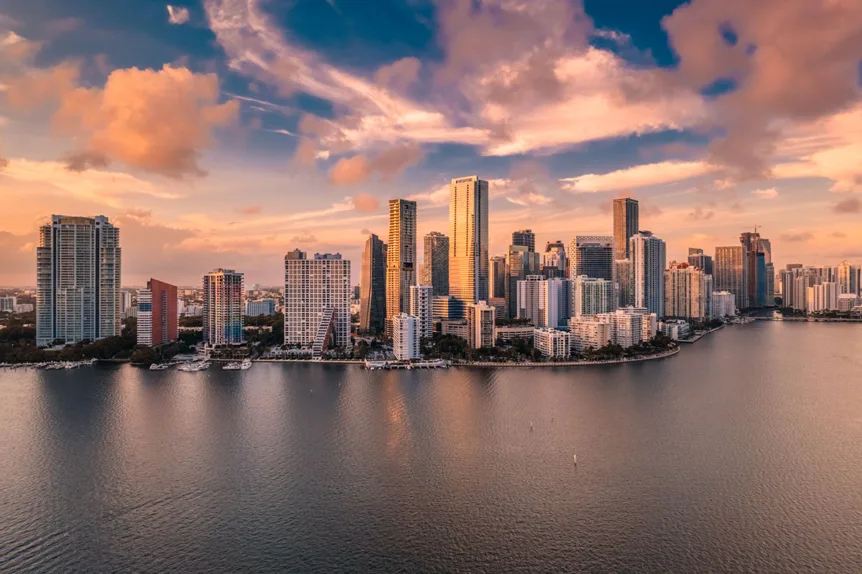 Aerial view of Miami skyline during sunset, showcasing the city's iconic high-rises and scenic waterfront, as seen from a Fair Lifts Helicopter Service flight.