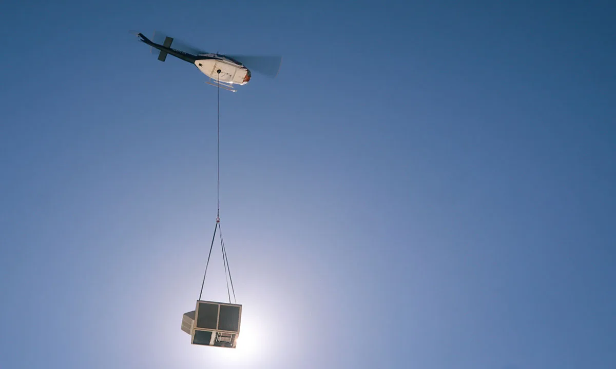 Huey helicopter lifting a 3500 pound HVAC rooftop unit with longline to the top of Hanwha Solar warehouse