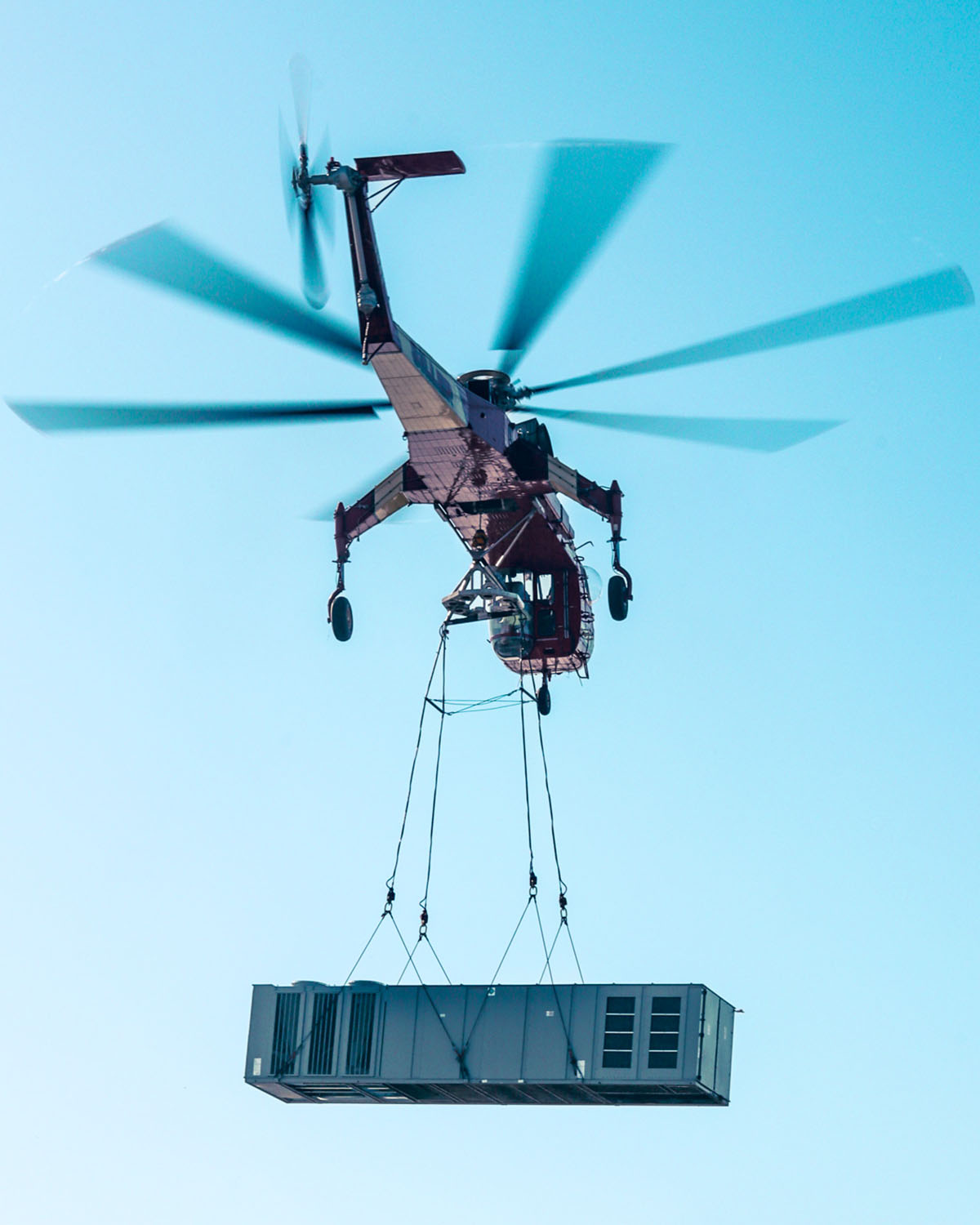Fair Lifts' precision airlift solutions featuring a Sikorsky S-64E flying above the project site, deploying an RTU onto the manufacturing plant roof.