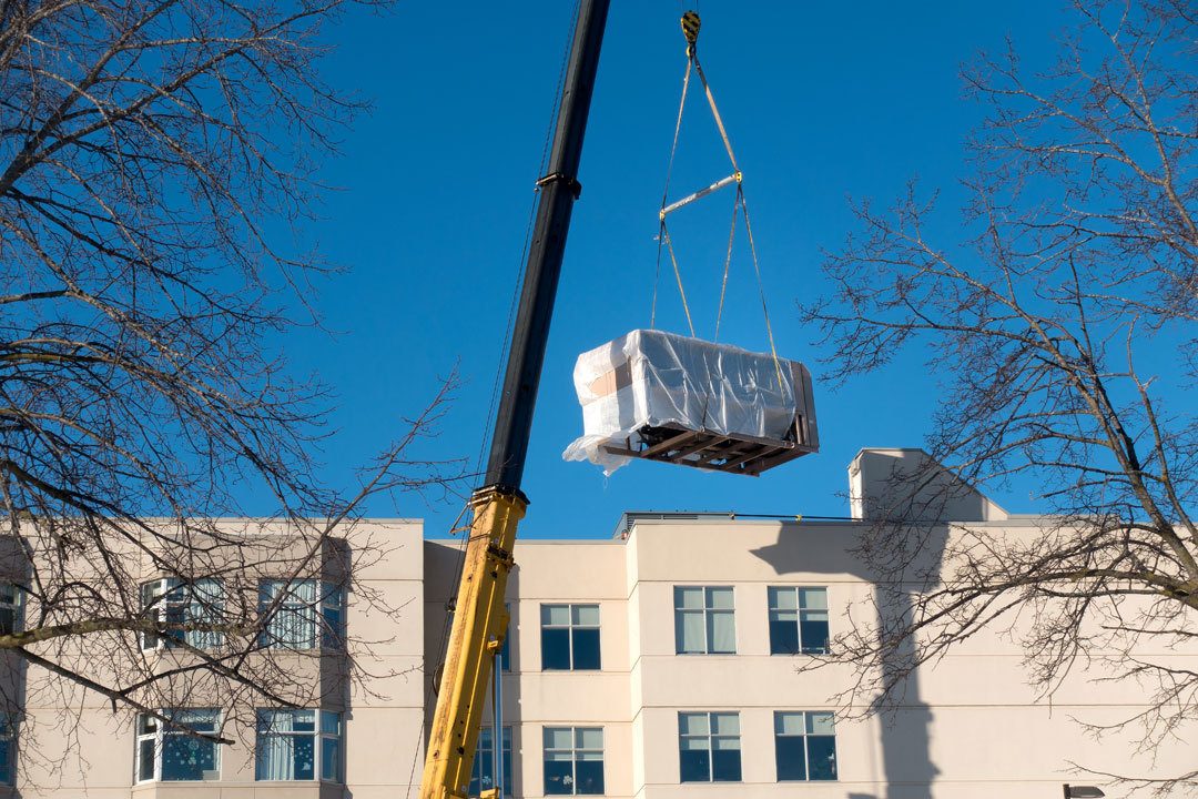 A ground crane lifts an HVAC root top unit.