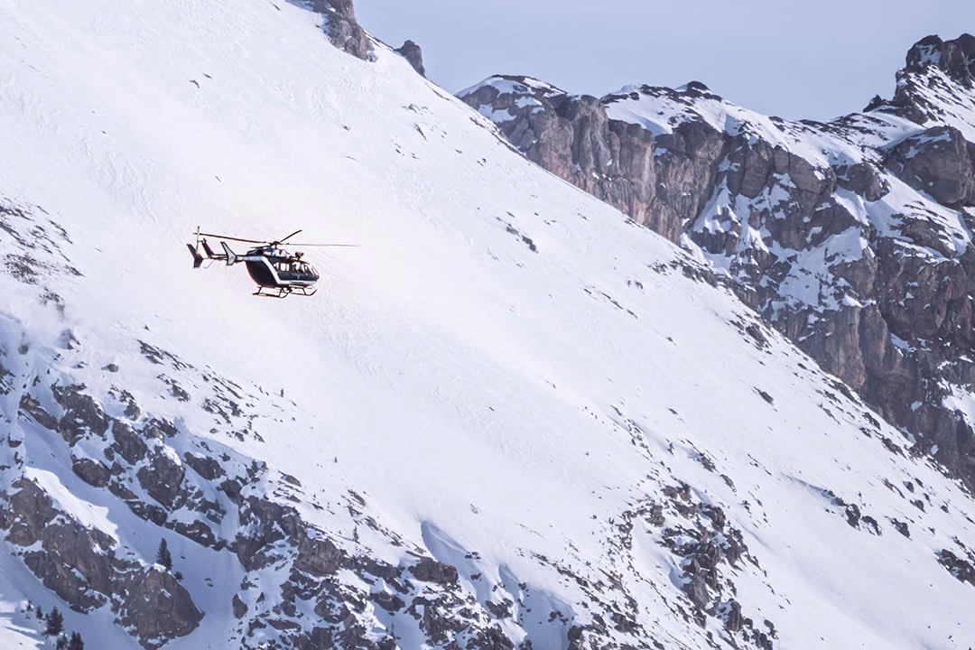 A rescue helicopter flies near steep, snow-covered peaks at Serre Chevalier, Briançon in the French Alps