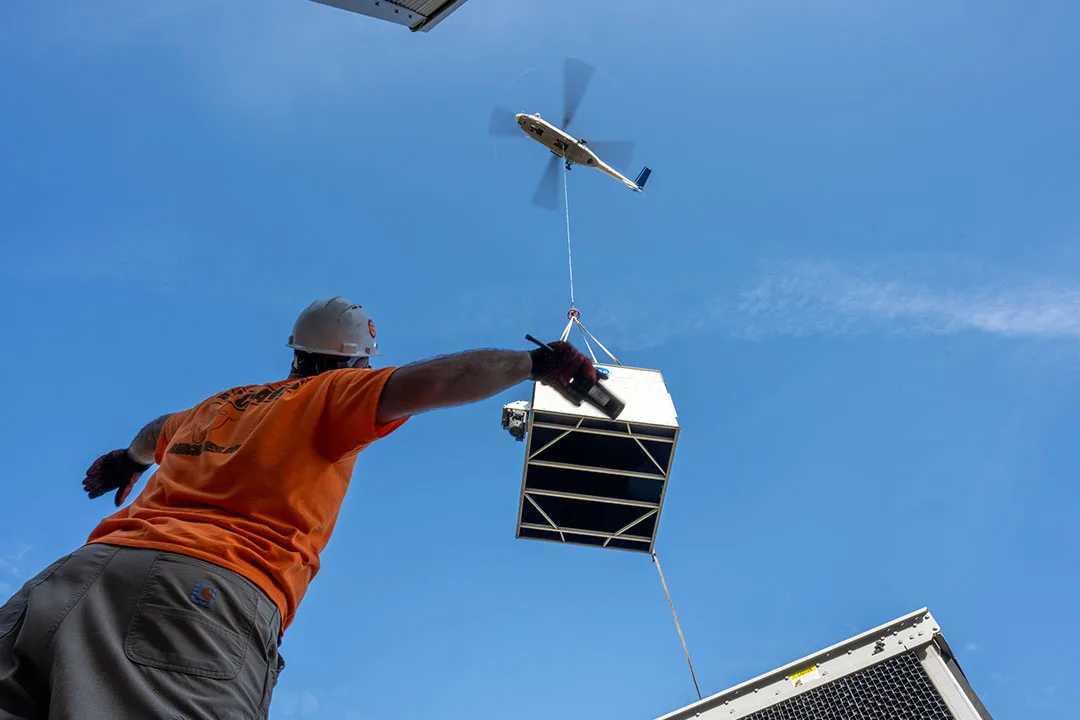 An HVAC unit being positioned into place by a helicopter crane.