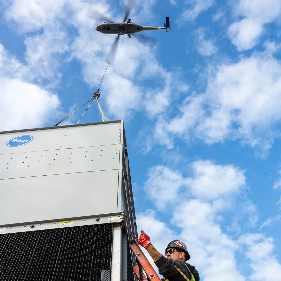 A helicopter crane lift crew member installs an HVAC rooftop unit.