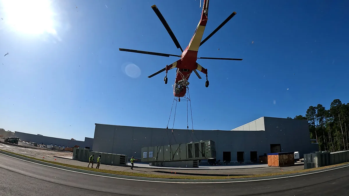 Sikorsky S-64 Skycrane lifting a commercial rooftop HVAC unit while rigging crew monitors the heavy lift operation