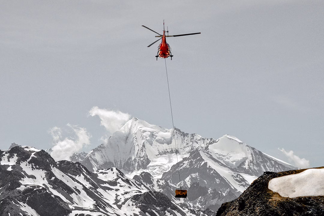 A helicopter delivers supplies, over the Swiss Alps in early summer.