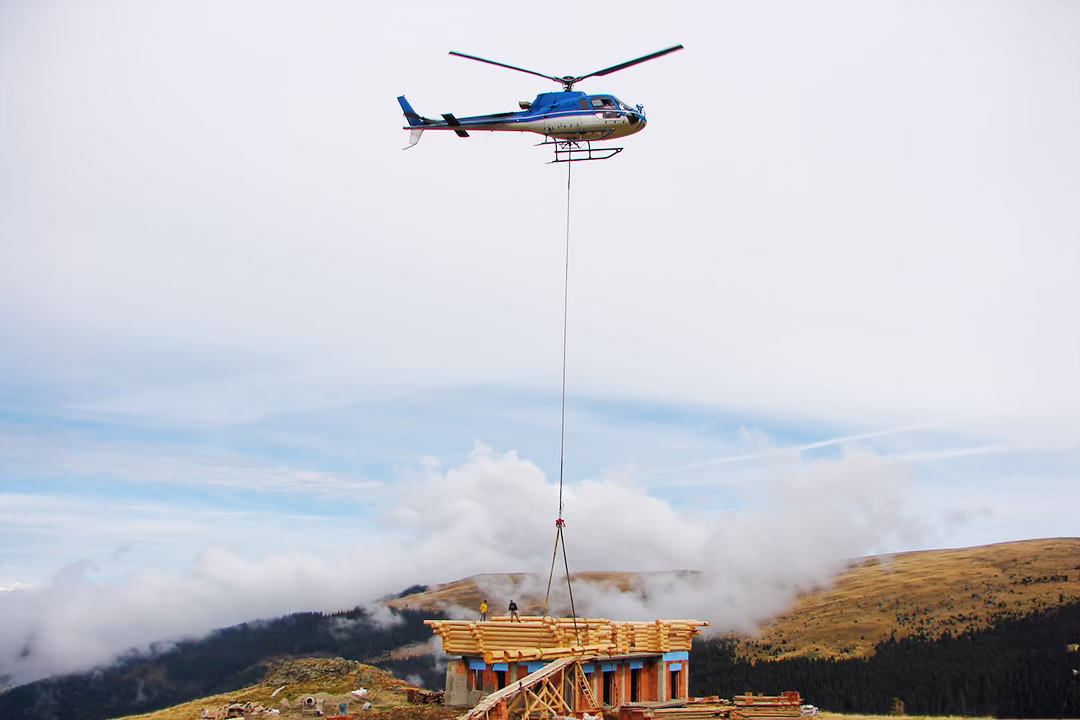 A helicopter places building materials to a remote construction site. 