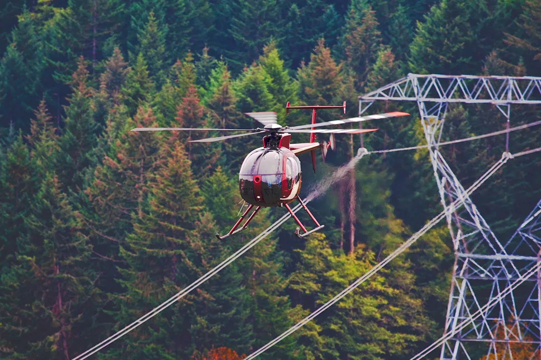 A helicopter hovers close to a high voltage line tower.