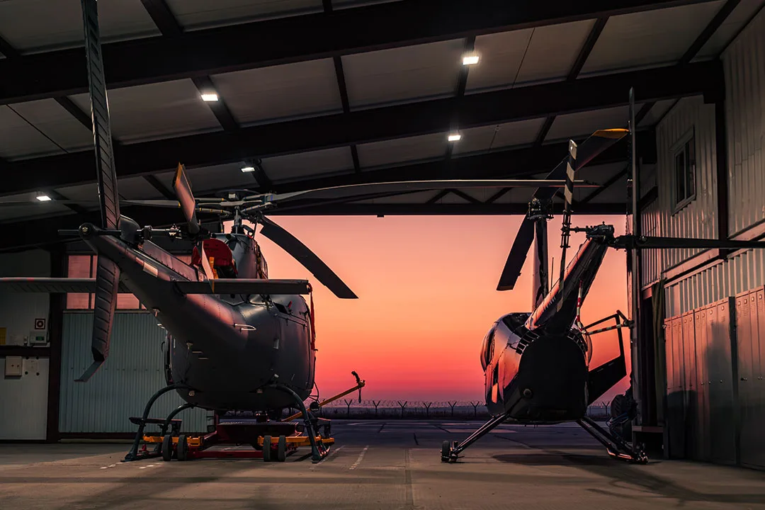 Two helicopters staged inside a hangar at sunset, ready for time-sensitive missions when conditions support safe night flight.