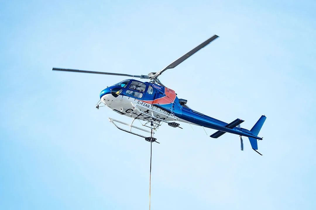 An Airbus H125 Helicopter conducting a precision sling load operation with a long line attached, captured mid-flight during an external load mission.