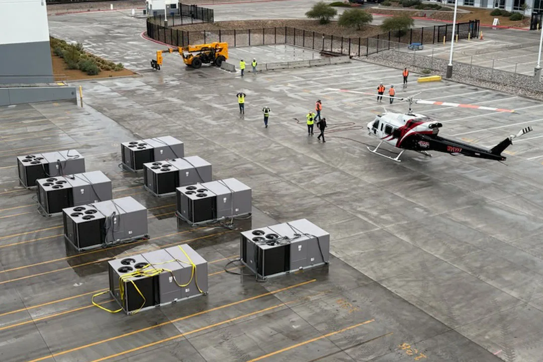Staging area with multiple HVAC units arranged on a rooftop parking deck as a helicopter prepares for sequential aerial crane lifts with coordinated ground crew support.