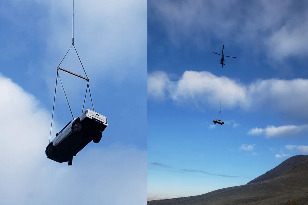 Side-by-side images showing a helicopter performing a vehicle recovery lift, with a pickup truck suspended beneath a long-line rigging system against a blue sky and mountainous terrain in the background.