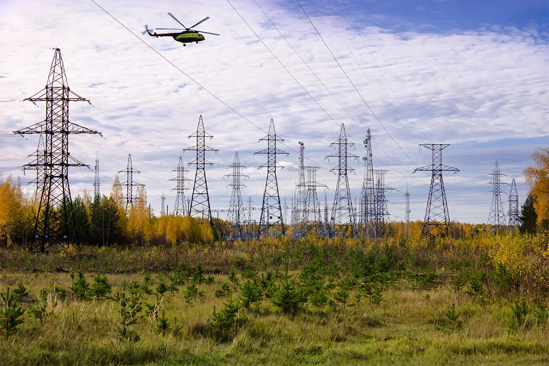 Helicopter conducting powerline patrol over high-voltage transmission towers and corridor landscape.