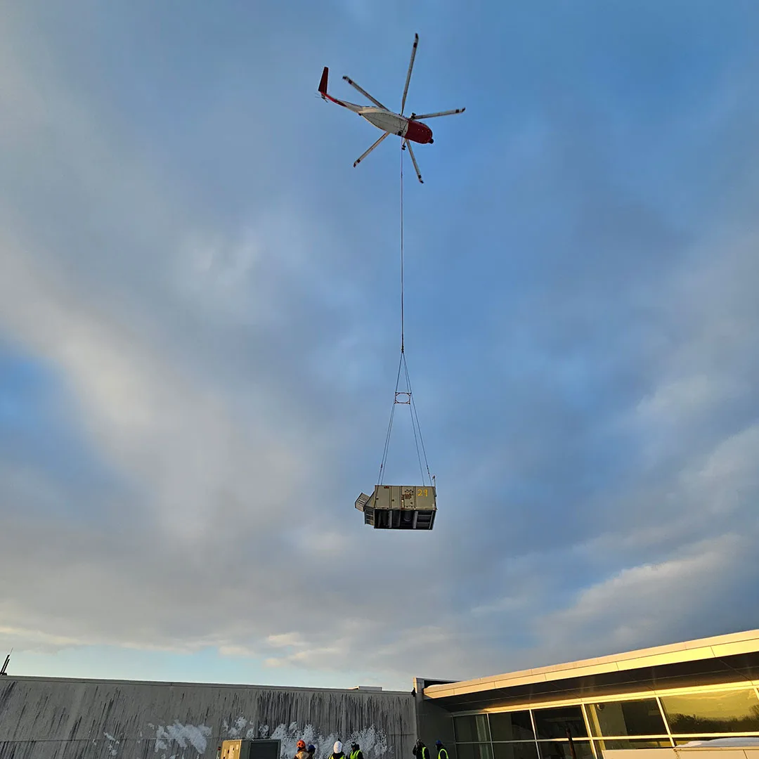 Sikorsky S-61N heavy lift helicopter hovering over a commercial building during a rooftop HVAC replacement project.