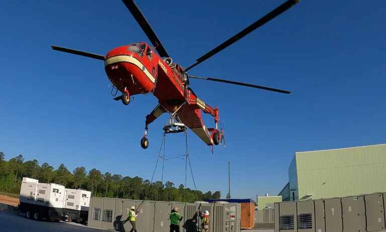 The Sikorsky S-64E helicopter hovering above a large HVAC unit prior to lifting.