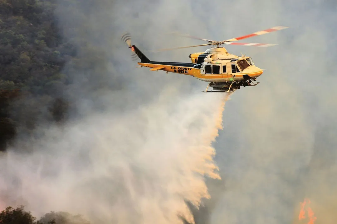 A Bell 412 Helitak firefighting helicopter releasing a high-volume water drop over an active wildfire. | Photo: bellflight.com