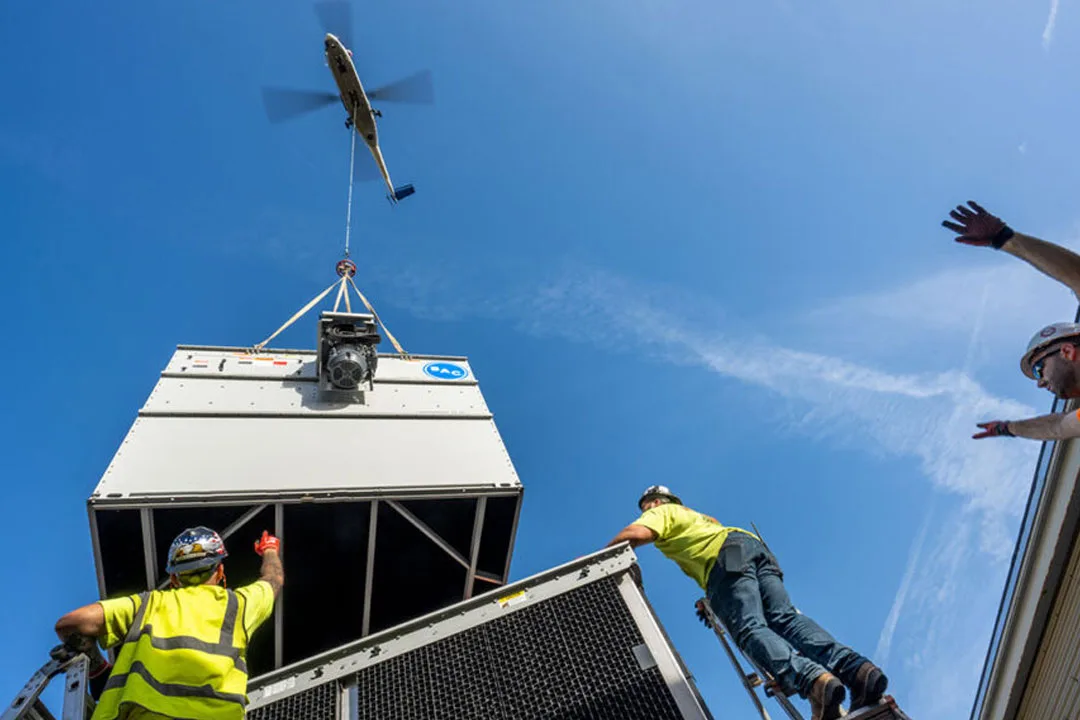 A helicopter positions a rooftop unit into place with guidance from the lift crew.