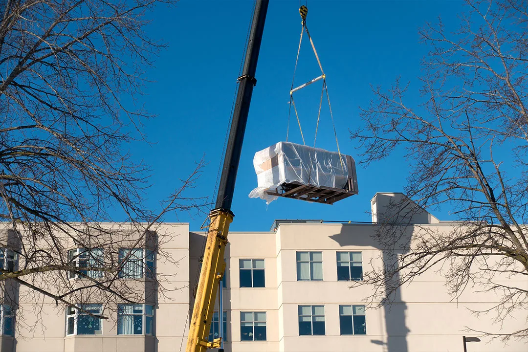 A ground crane positions an HVAC unit onto a roof top.