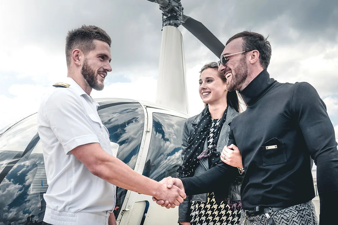 A helicopter charter pilot greets VIP festival travelers beside a private helicopter before departure.