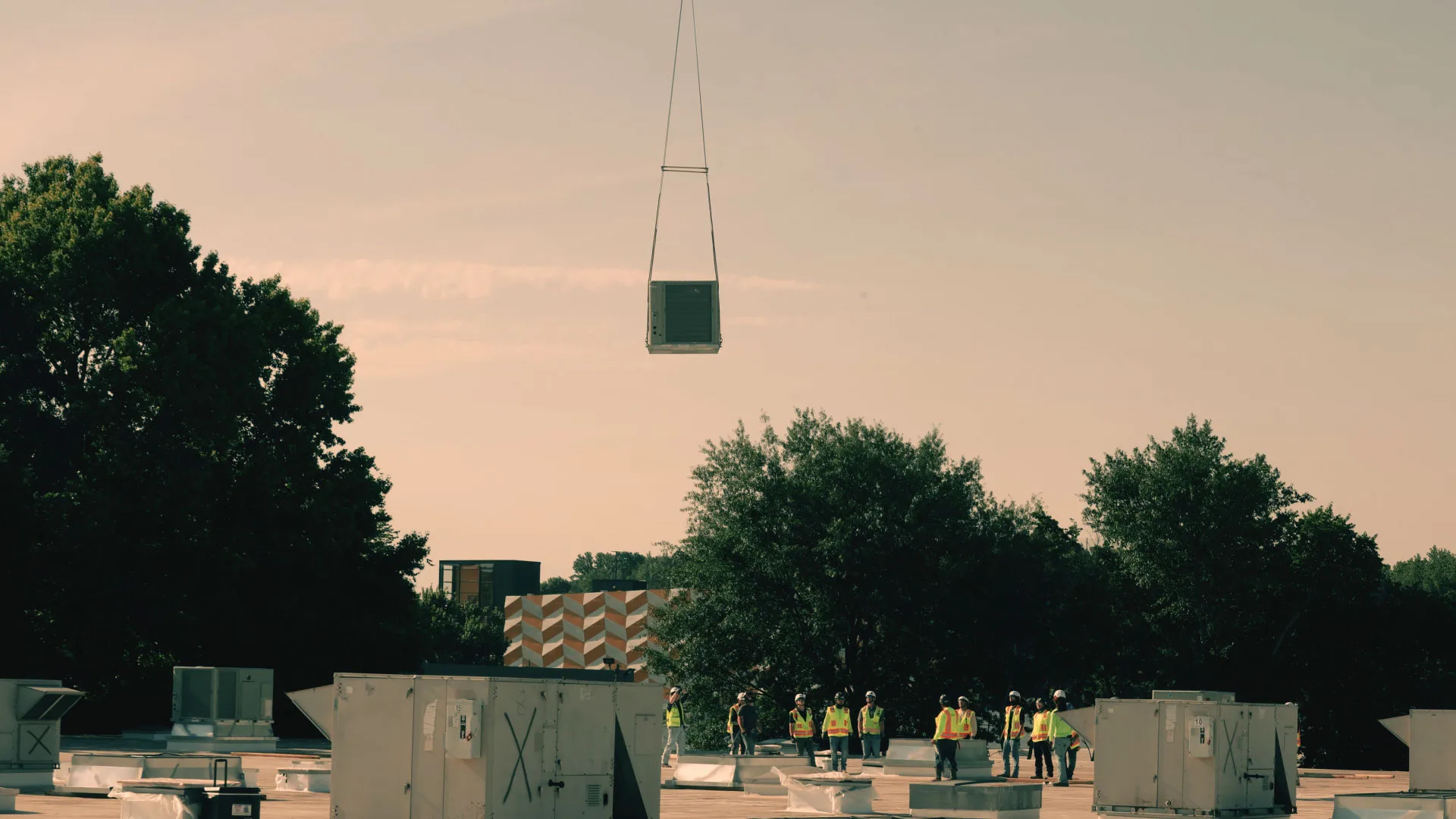 An HVAC unit suspended in the air by a helicopter above technicians on an Atlanta roof.