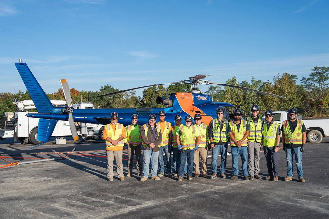 Helicopter lifting crew wearing high-visibility safety vests standing in front of an Airbus AS350 helicopter.